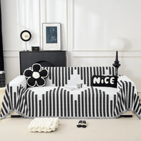 Zwart-wit gestreepte bankhoes met franjes over een bank, gestyled met bloemvormig kussen, tekstkussen, tijdschrift en kopje in een witte kamer. 1