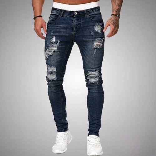 Voorkant van slim fit jeans met scheuren in donkerblauw verweerd denim, gedragen door een model met witte sneakers. 4