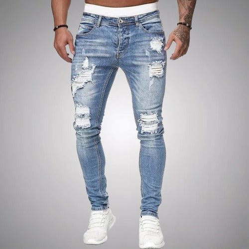 Voorkant van slim fit jeans met scheuren in lichtblauw verweerd denim, gedragen door een model met witte sneakers. 2