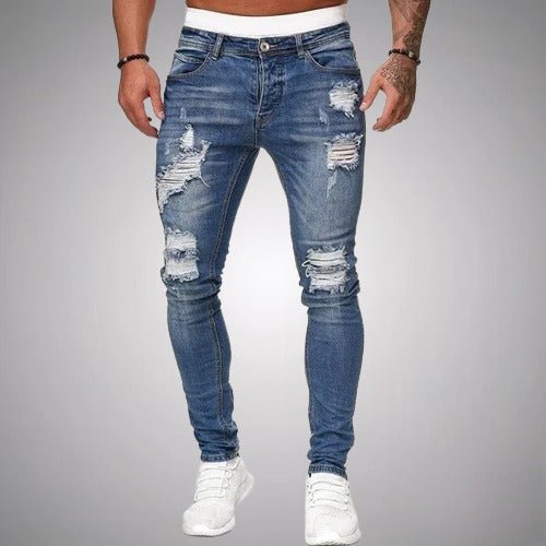 Voorkant van slim fit jeans met scheuren in middenblauw verweerd denim, gedragen door een model met witte sneakers. 3