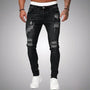 Voorkant van slim fit jeans met scheuren in zwart verweerd denim, gedragen door een model met witte sneakers. 1