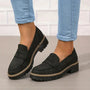 Zwarte loafers met dikke profielzool gedragen onder opgerolde blauwe jeans, één voet schuin gedraaid. 6