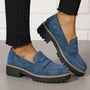 Blauwe suèdelook loafers met zwarte profielzool gedragen met zwarte broek, één voet opgetild met zijaanzicht van de zool. 9