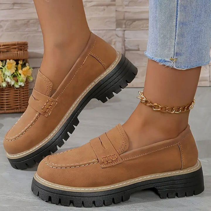 Bruine suèdelook loafers met zwarte profielzool en bruine stiksels, gedragen met gouden enkelbandje en jeans. 17
