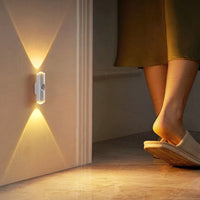 Wandlamp naast een deurpost die 's avonds warm licht geeft, met voeten in slippers op de vloer 13