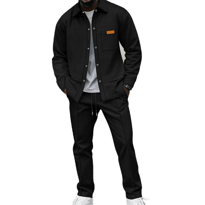 Man draagt de wafelgebreide set in zwart, overhemd open over grijs shirt, handen in zakken 1