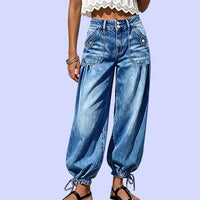 Voorkant van de blauwe barreljeans met hoge taille, dubbele knoopsluiting, opgestikte zakken en strikkoorden aan de zoom, tegen lila achtergrond. 10