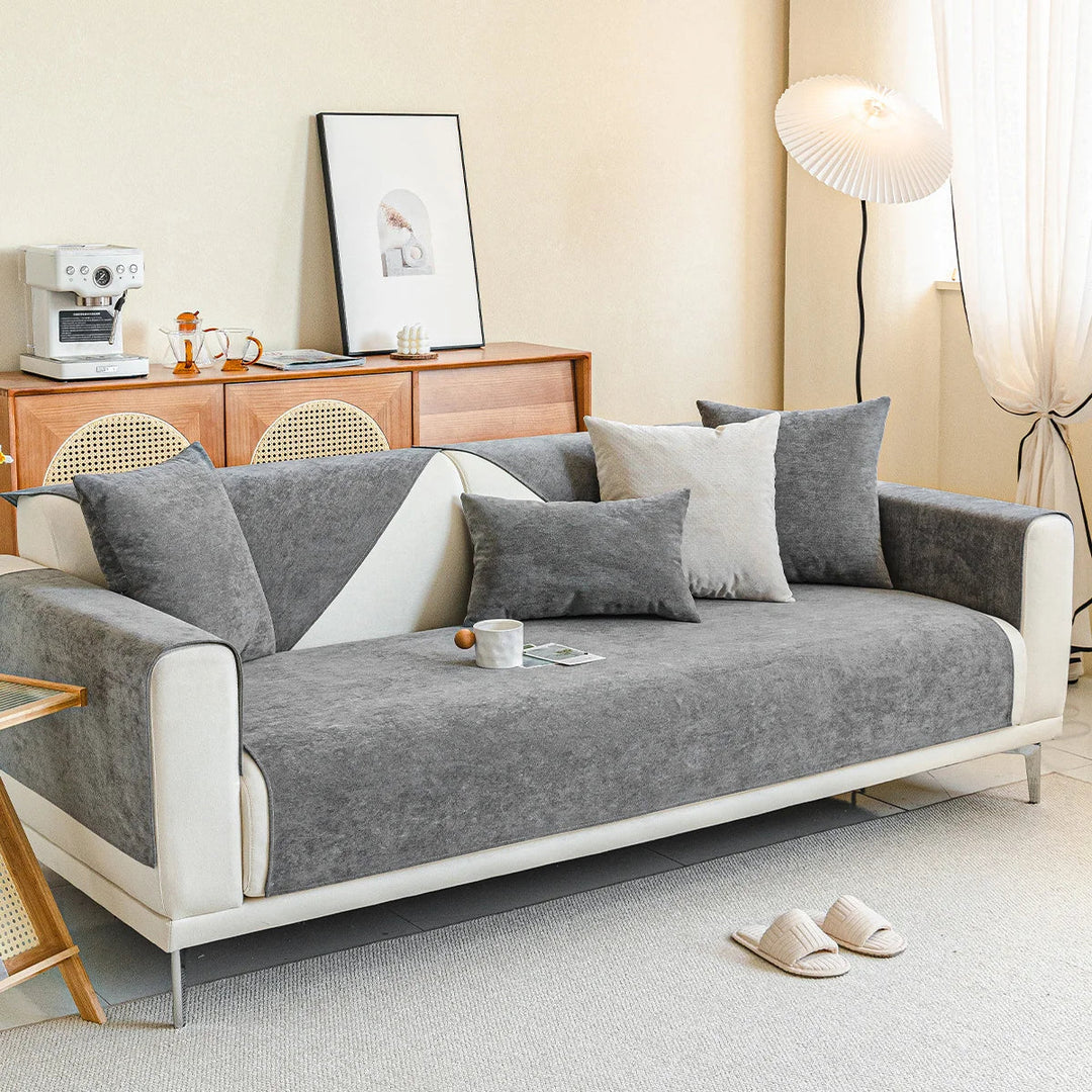 Grijze bankhoes op een witte bank in een woonkamer met houten dressoir, koffiemachine, staande lamp en pantoffels. 13