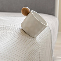 Een wit kopje met houten bol balanceert op de rand van een bank met antislip stippen op de hoes. 7