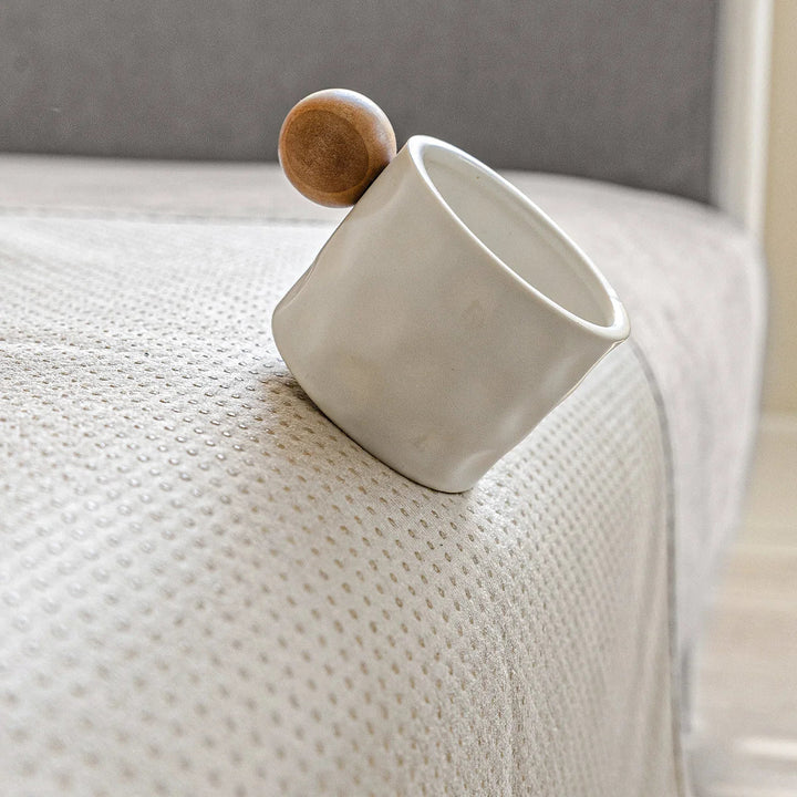 Een wit kopje met houten bol balanceert op de rand van een bank met antislip stippen op de hoes. 7