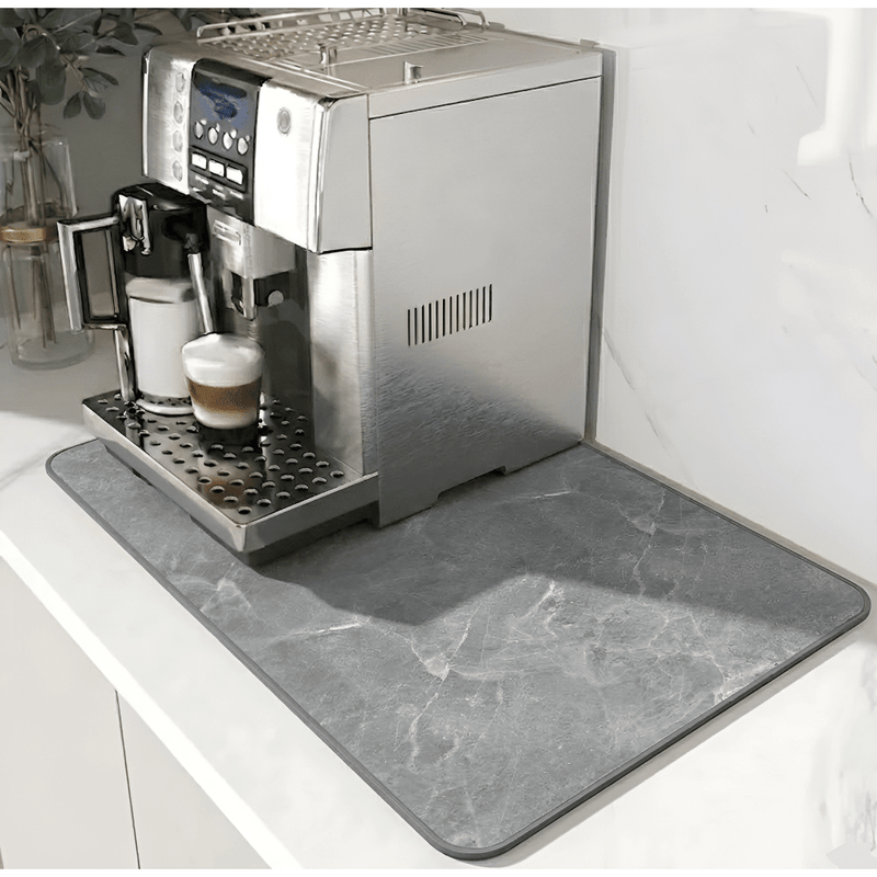 Mat met grijze marmerlook en donkere rand onder een zilverkleurige koffiemachine op een wit aanrechtblad. 12