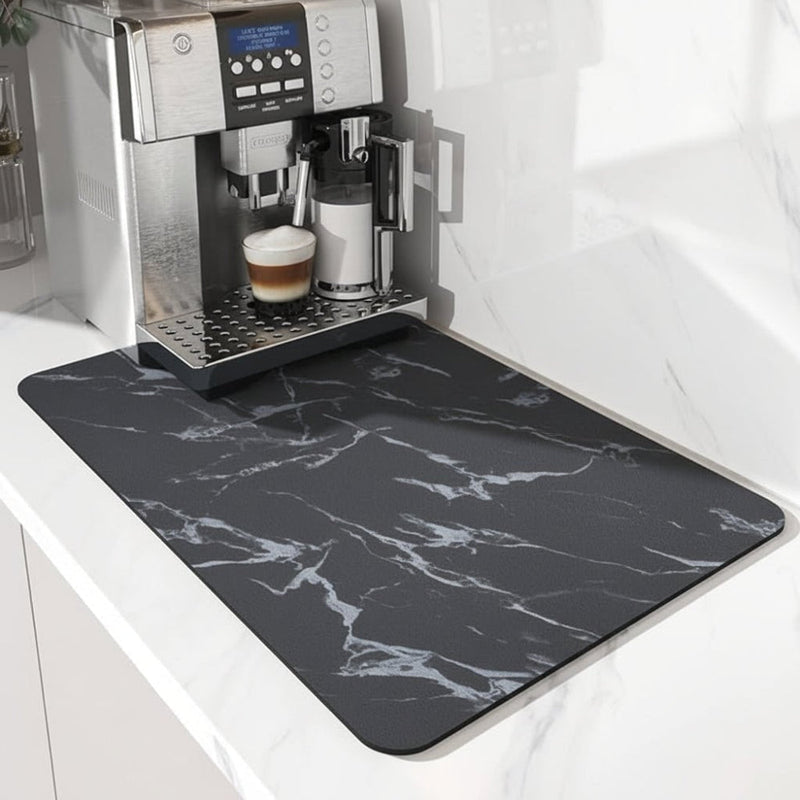 Zwarte mat met witte marmerlook-aders onder een koffiemachine, schuin van opzij gefotografeerd op een wit blad. 4