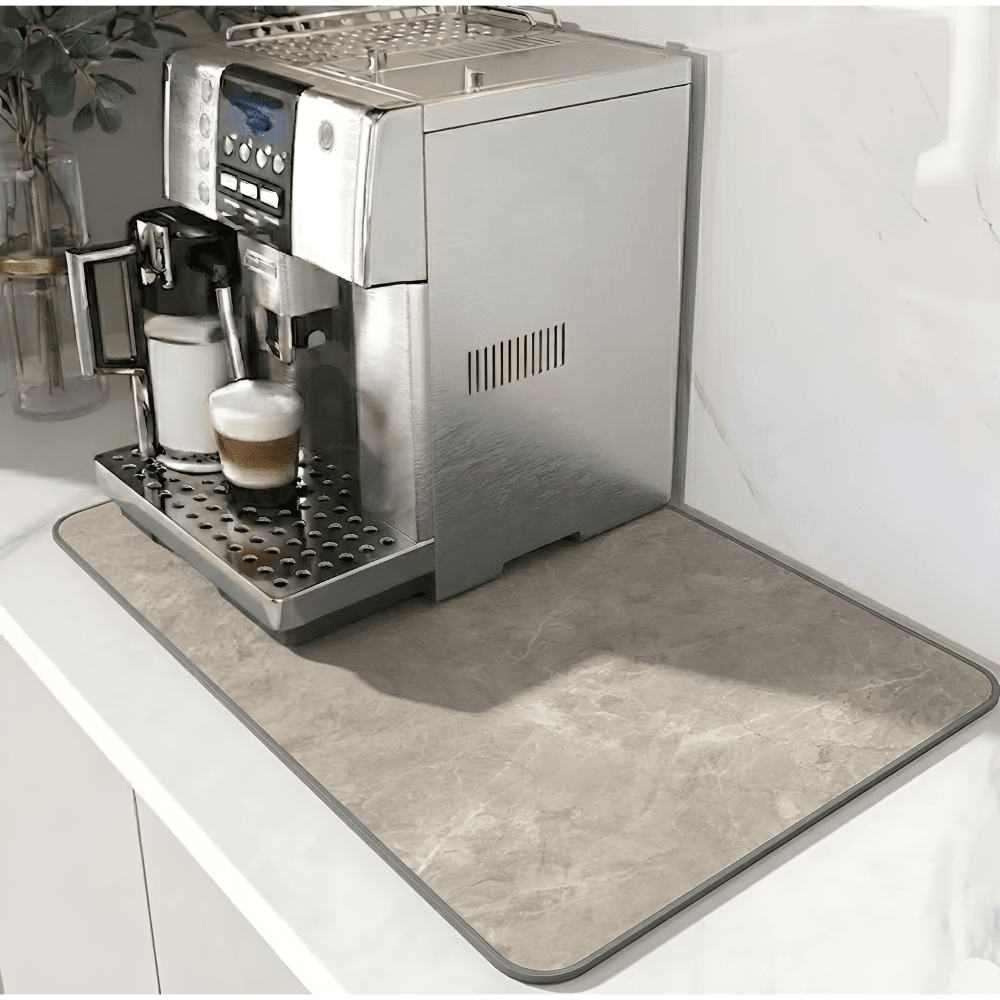 Mat met beige steenlook en grijze rand onder een koffiemachine op een wit aanrecht. 11