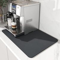 Donkergrijze mat onder een volautomatische koffiemachine op een wit marmeren aanrecht, gezien vanaf de voorzijde. 2