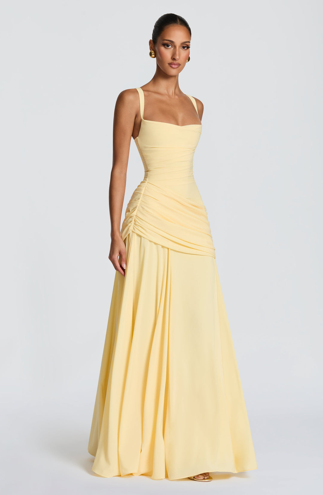 Model in de lichtgele maxi-jurk, driekwart van opzij, met de geplooide drapering rond de heupen en de vloeiende, wijd vallende chiffon rok. 3