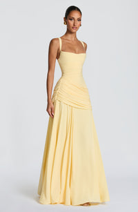 Model in de lichtgele maxi-jurk, driekwart van opzij, met de geplooide drapering rond de heupen en de vloeiende, wijd vallende chiffon rok. 3