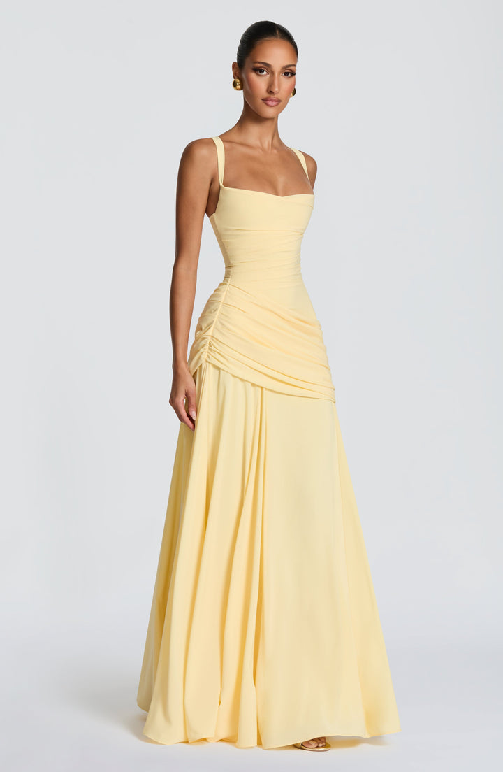 Model in de lichtgele maxi-jurk, driekwart van opzij, met de geplooide drapering rond de heupen en de vloeiende, wijd vallende chiffon rok. 3