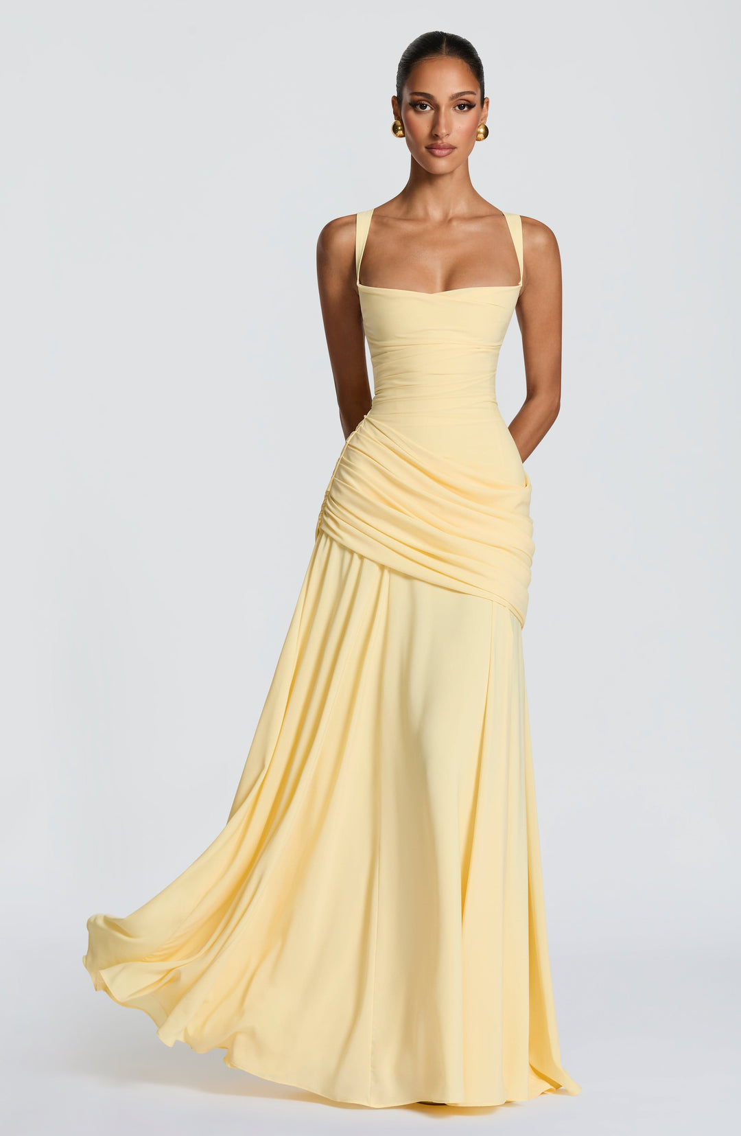 Model draagt de lichtgele chiffon maxi-jurk van voren, met vierkante halslijn, gedrapeerde heuppartij en wijd uitwaaierende rok in beweging. 1
