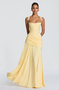 Model draagt de lichtgele chiffon maxi-jurk van voren, met vierkante halslijn, gedrapeerde heuppartij en wijd uitwaaierende rok in beweging. 1