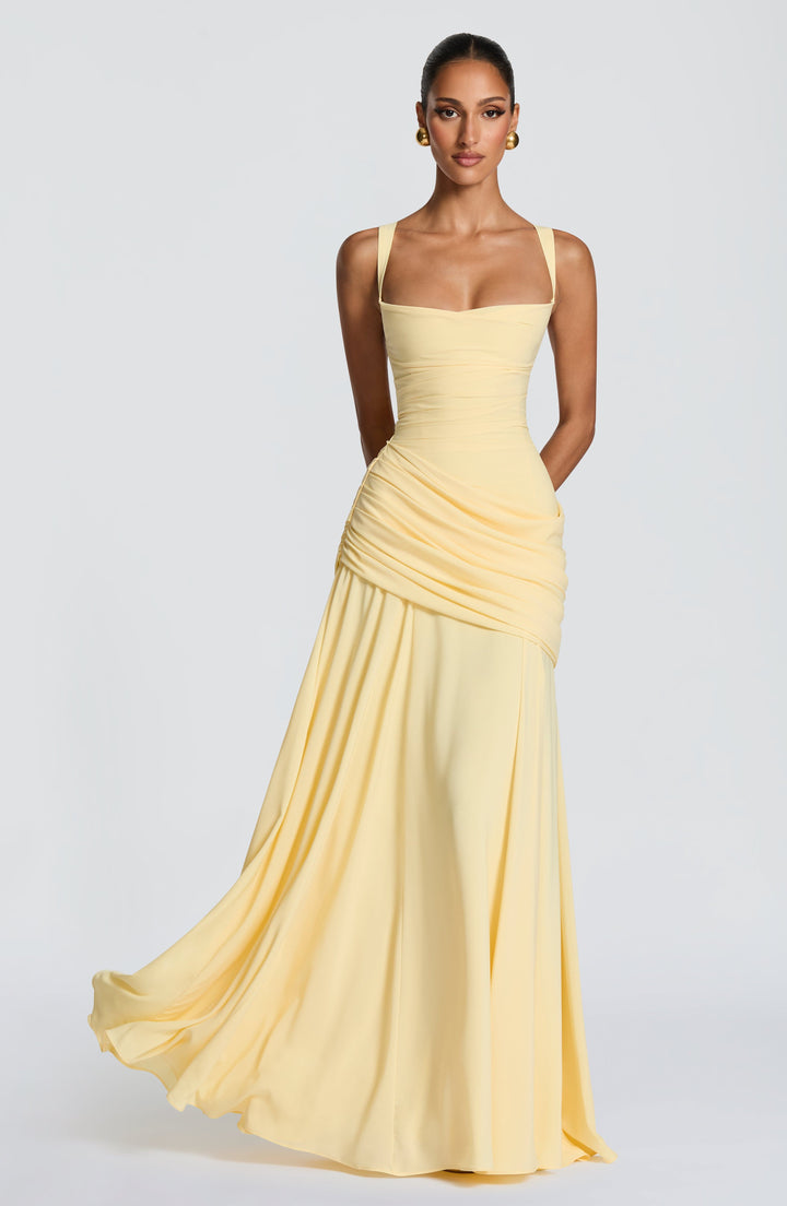 Model draagt de lichtgele chiffon maxi-jurk van voren, met vierkante halslijn, gedrapeerde heuppartij en wijd uitwaaierende rok in beweging. 1