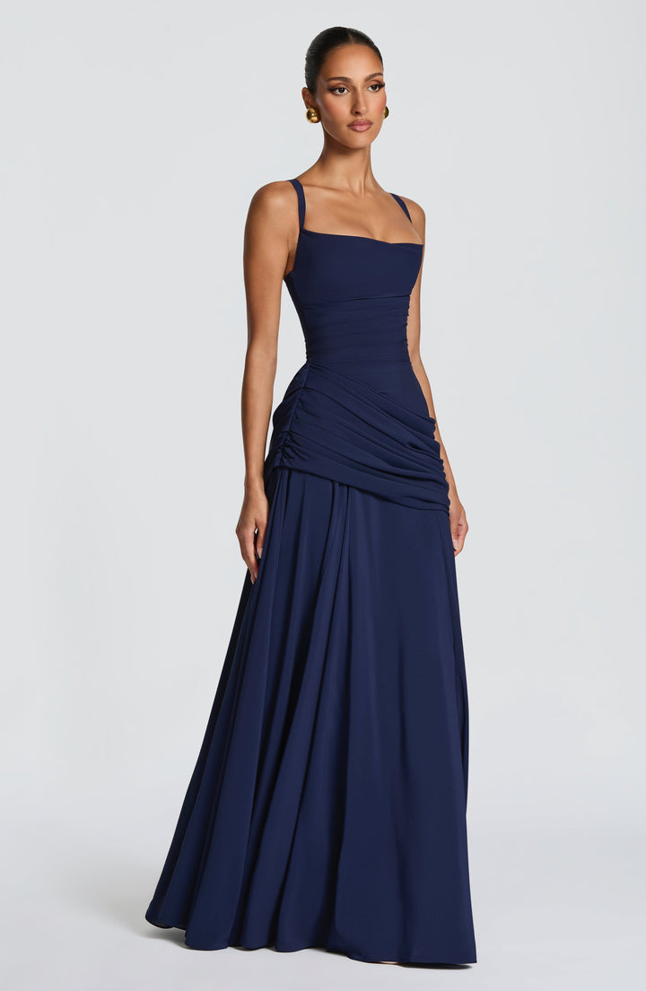 Model in de marineblauwe jurk, driekwart zijaanzicht, met dunne schouderbandjes, geplooide taille en wijd uitlopende chiffon rok. 12