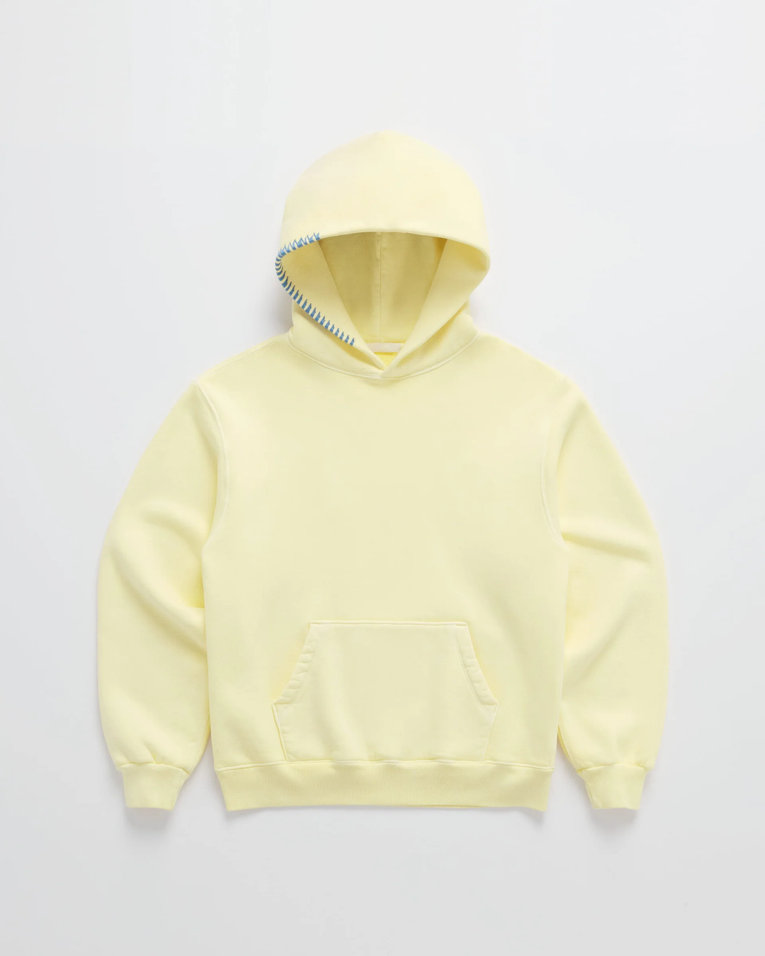Hoodie in zachtgeel van voren op een lichte achtergrond, met blauwe stiksels langs de rand van de capuchon en een buidelzak. 1