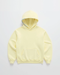 Hoodie in zachtgeel van voren op een lichte achtergrond, met blauwe stiksels langs de rand van de capuchon en een buidelzak. 1