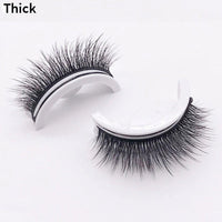 Twee wimperstukjes met dikke, volle donkere wimpers op witte houdertjes, liggend op een lichte achtergrond, de variant dik. 12