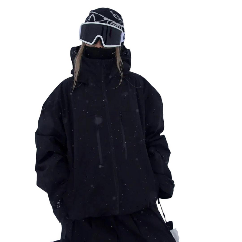 Zwarte snowjack gedragen door een model met muts en skibril, vooraanzicht met hoge kraag en handen in de zakken. 3