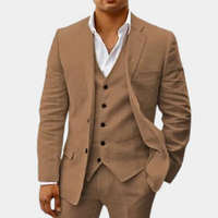 Model draagt het pak in bruin met gilet, wit overhemd met open kraag en een hand in de zak. 2