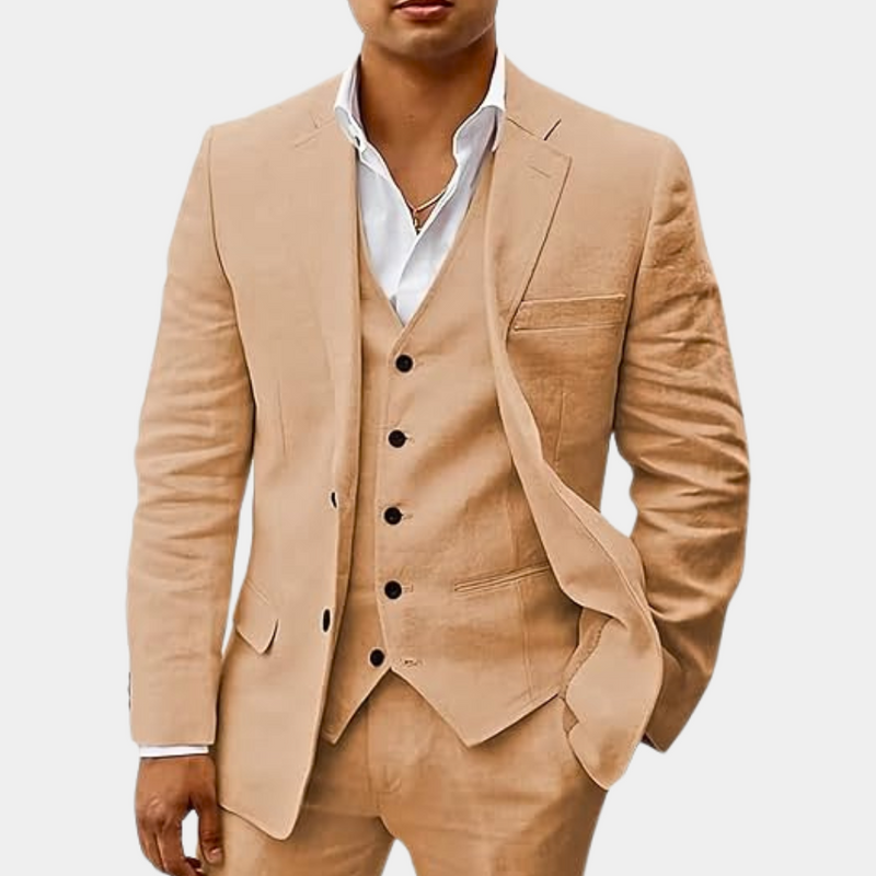 Model draagt het pak in zandkleur met vijfknoops gilet, wit overhemd en een hand in de broekzak. 3