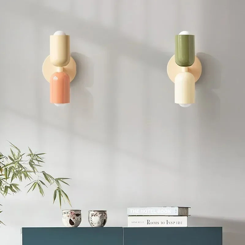 Twee wandlampen in crème-perzik en groen-crème naast elkaar boven een blauwgroen dressoir met kopjes, boeken en bamboeplant. 14