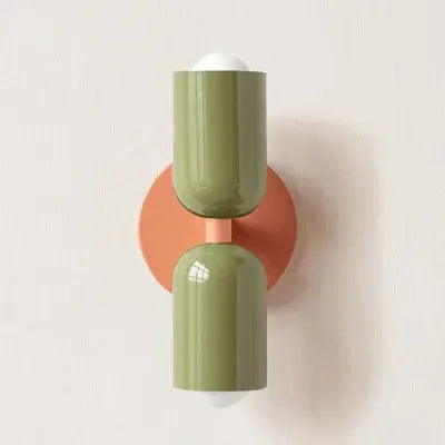 Wandlamp met twee glanzende groene kappen op een ronde oranje wandplaat, tegen een lichte muur. 21