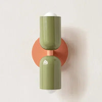 Wandlamp met twee glanzende groene kappen op een ronde oranje wandplaat, tegen een lichte muur. 21