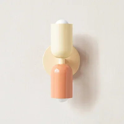 Wandlamp in crème en perzikroze met crèmekleurige wandplaat, close-up tegen een lichte muur. 16