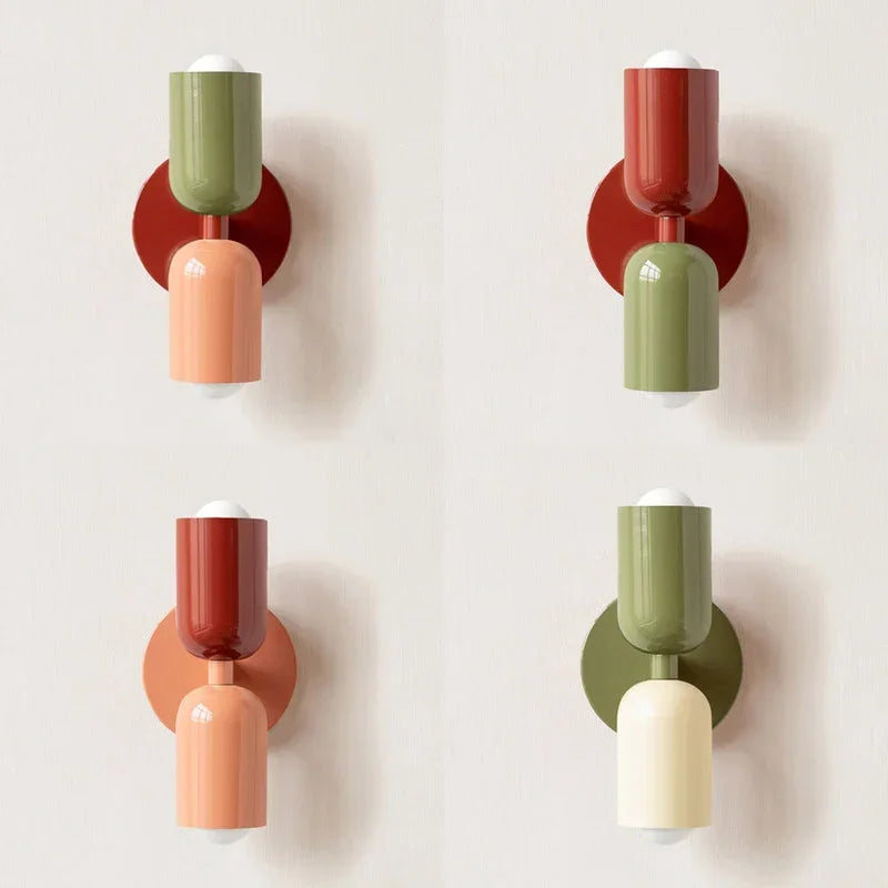 Vier wandlampen in verschillende kleurcombinaties van groen, rood, perzik en crème naast elkaar tegen een lichte muur. 12