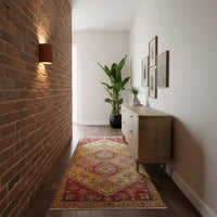 Terracotta wandlamp die een bakstenen muur in een gang met kleed en dressoir verlicht 4