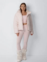 Volledig vooraanzicht van model in open roze pufferjack met bijpassende legging en bontlaarzen 10
