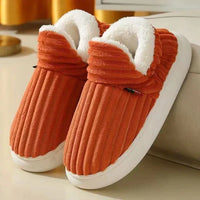 Oranje geribbelde pluchen pantoffels met witte fleece voering en dikke witte zool, schuin neergezet naast een bank. 6