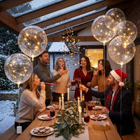 Gezelschap viert feest aan een houten tafel onder een glazen dak, omringd door lichtgevende ballonnen 2