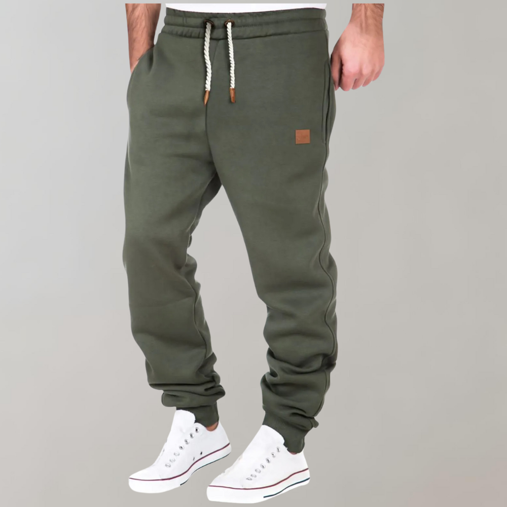 Legergroene joggingbroek gedragen door een model met een hand in de zak, wit koord en witte sneakers 3