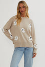 Model met blond haar draagt de beige trui met witte pluizige spookjes op borst en mouwen, gecombineerd met lichtblauwe jeans, frontaal gefotografeerd. 1