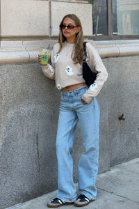 Model leunt tegen een stenen muur in de trui met spookjes, gedragen als korte trui met wijde jeans en sneakers. 3