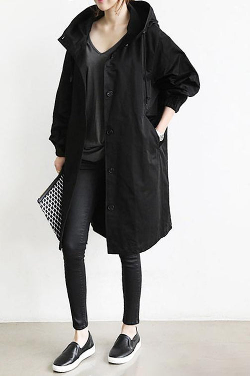 Zwarte lange regenjas met capuchon, open gedragen over een grijs shirt, met zwarte legging en sneakers 2
