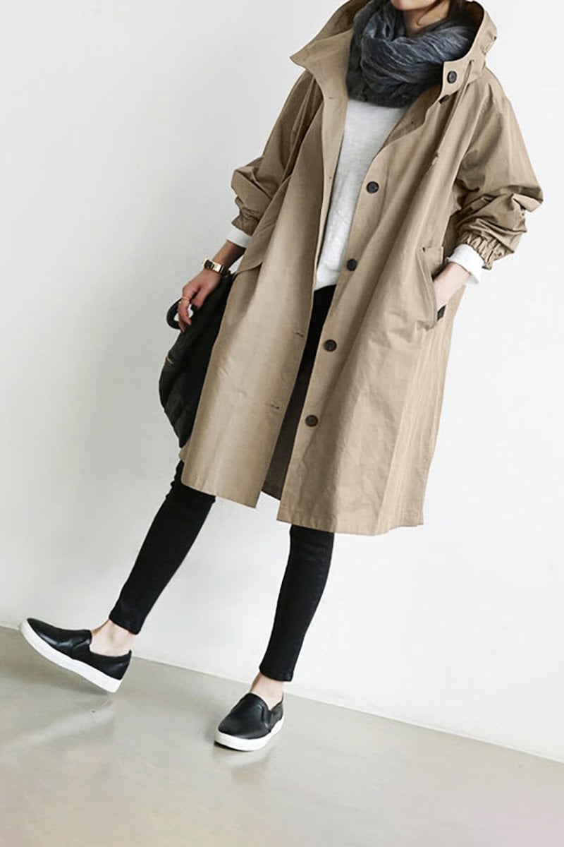 Beige lange regenjas met capuchon en knoopsluiting, gedragen met witte trui, grijze sjaal en zwarte legging 5