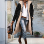 Model loopt buiten in de lange zwarte gewatteerde jas met open voorkant, zichtbare beige fleecevoering en capuchon, met jeans en handtas. 4