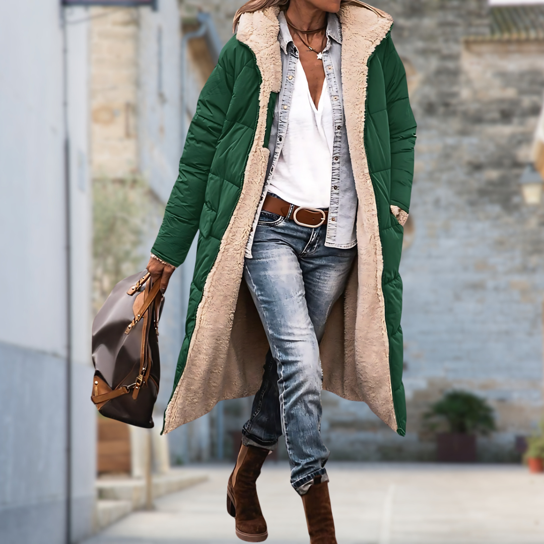 Model loopt door een straat in de lange gewatteerde jas in groen, open gedragen met beige fleecevoering aan de binnenkant. 7