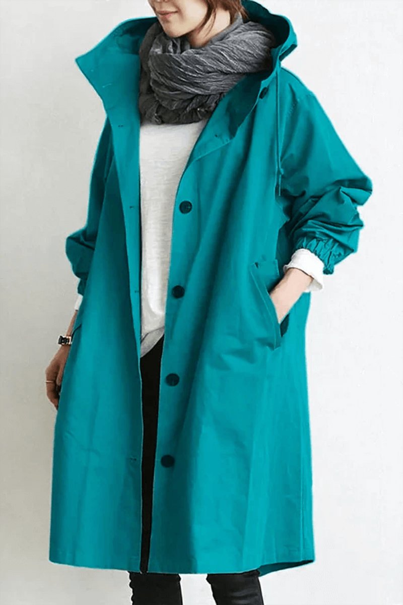 Turquoise lange jas met capuchon en drukknopen, gedragen met grijze sjaal, voorkant met hand in zak 2