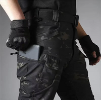 Detail van de camouflagebroek met rits-zakken op het been; een telefoon zit half in het vak, de riem is zichtbaar. 19